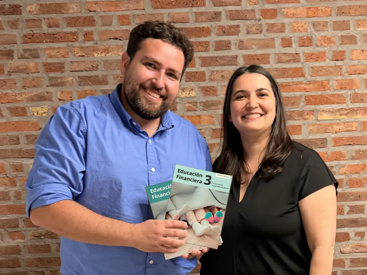 Francisco Ackermann y Macarena Bascour, sonrientes, muestran los cuadernillos de Educación Financiera 3